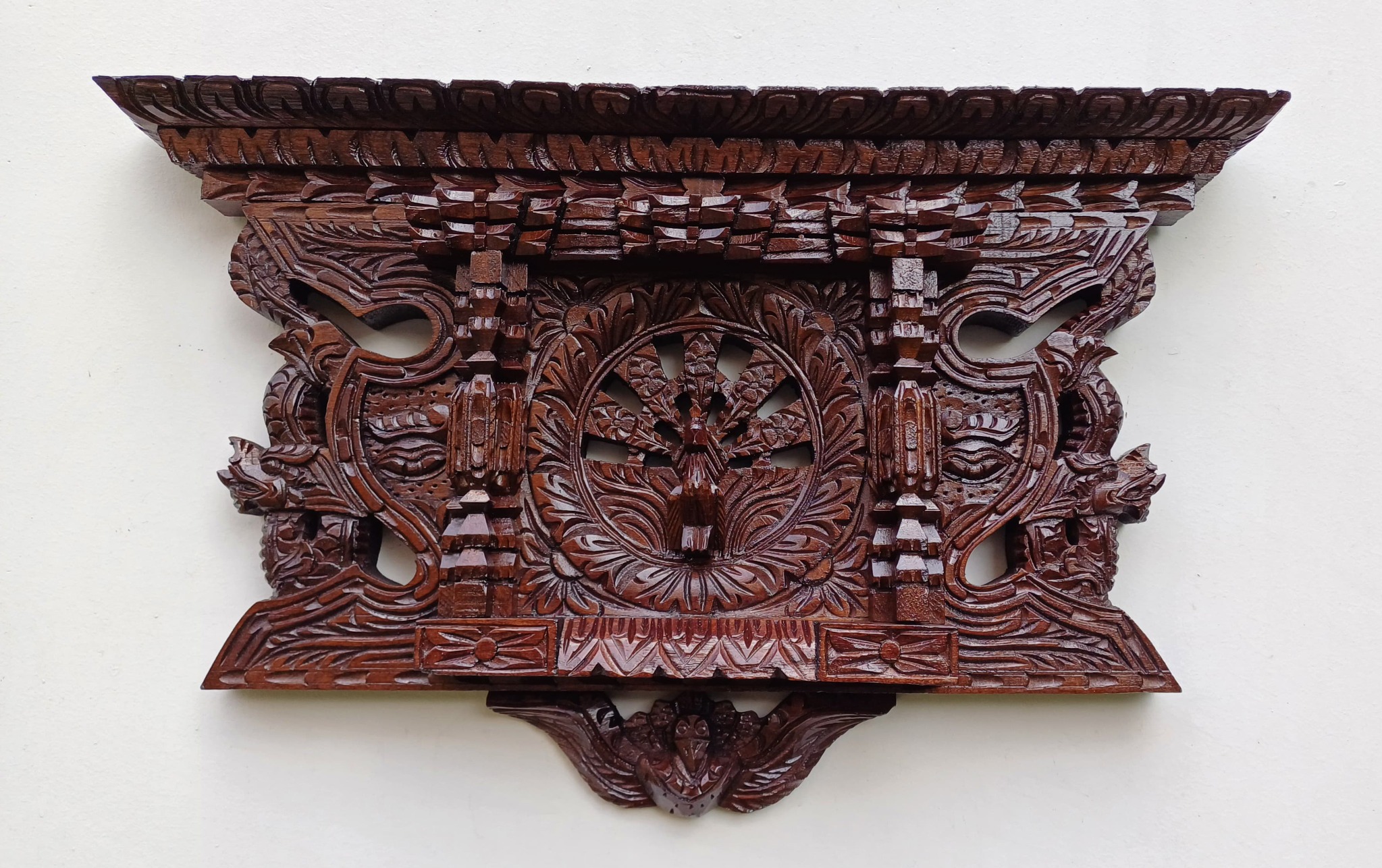 Intricately carved dark wooden decorative wall piece.