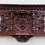 Dark carved wooden wall shelf or shrine with intricate traditional patterns.