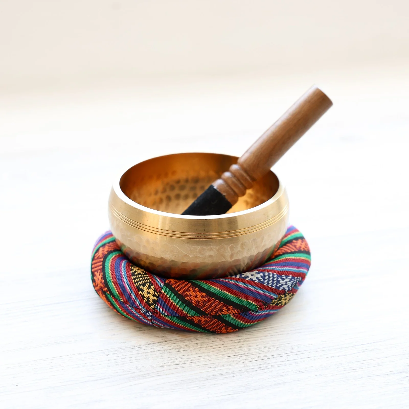 Handcrafted singing bowl with wooden mallet on a woven cushion.